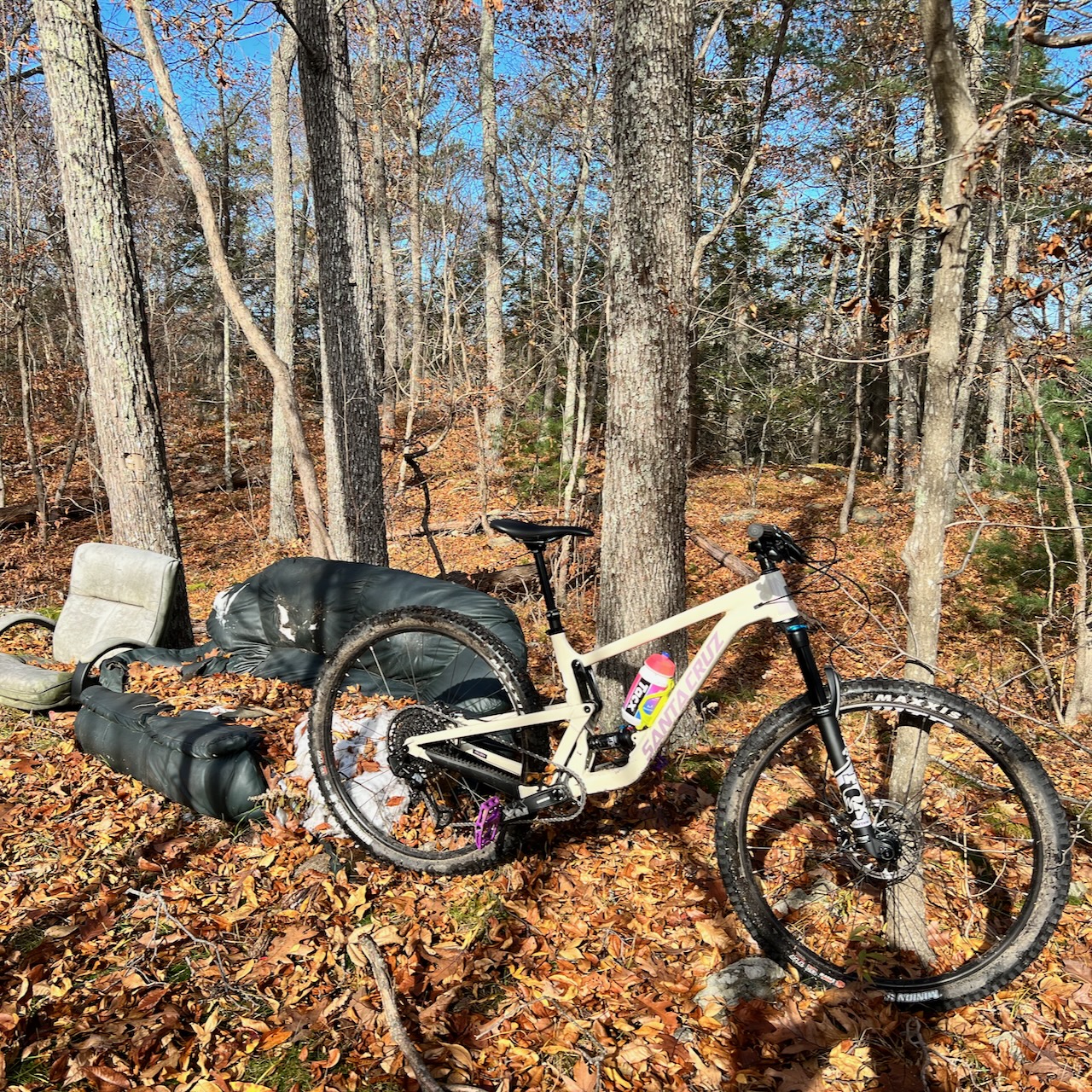 A mountain bike in the woods next to a beat up couch.